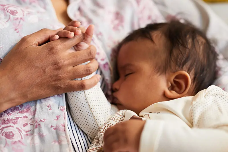 Jemand hält die Hand eines schlafendes Baby. 