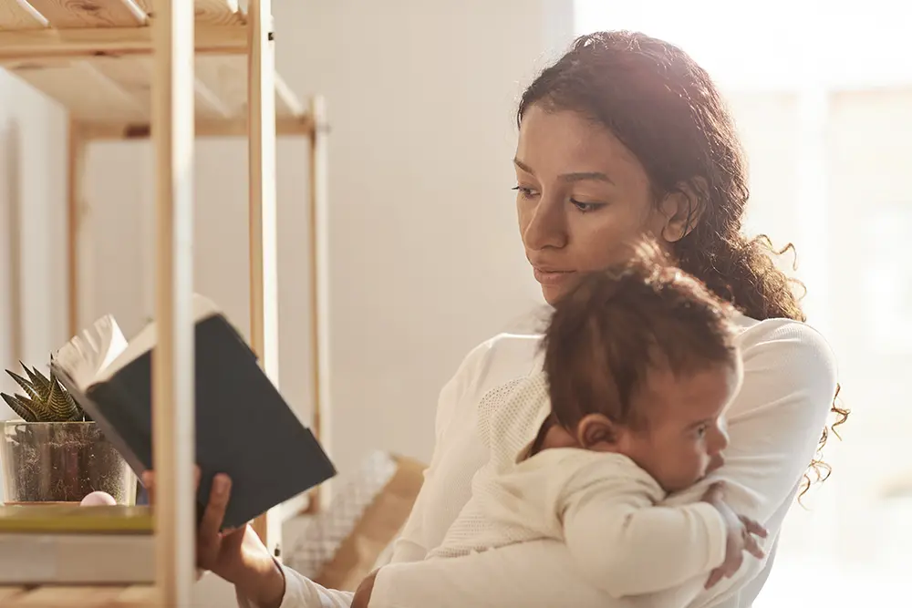 Mutter liest ein Buch während sie ihr Baby im Arm hält